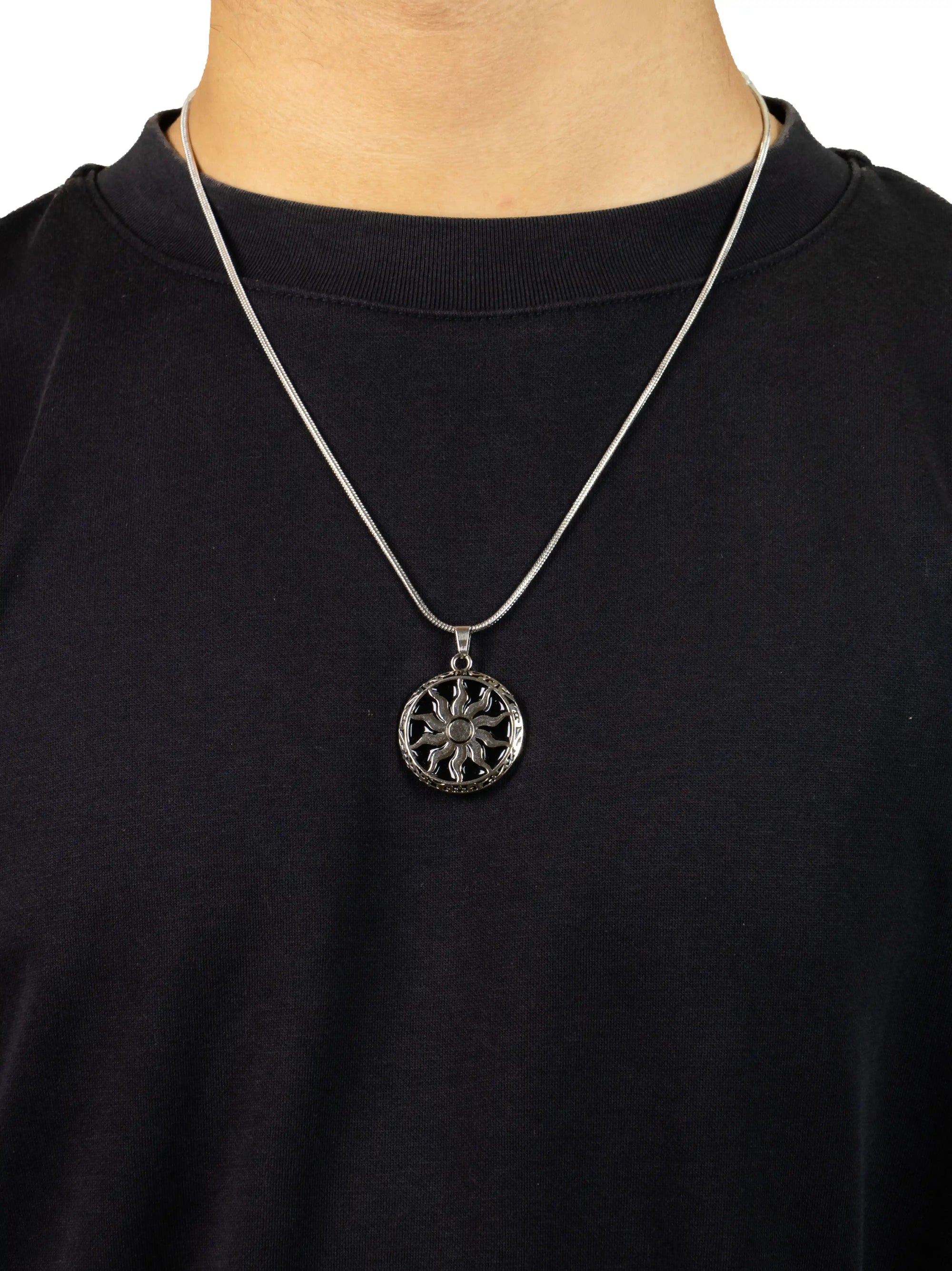 Person wearing a black shirt with a silver necklace featuring a circular pendant.