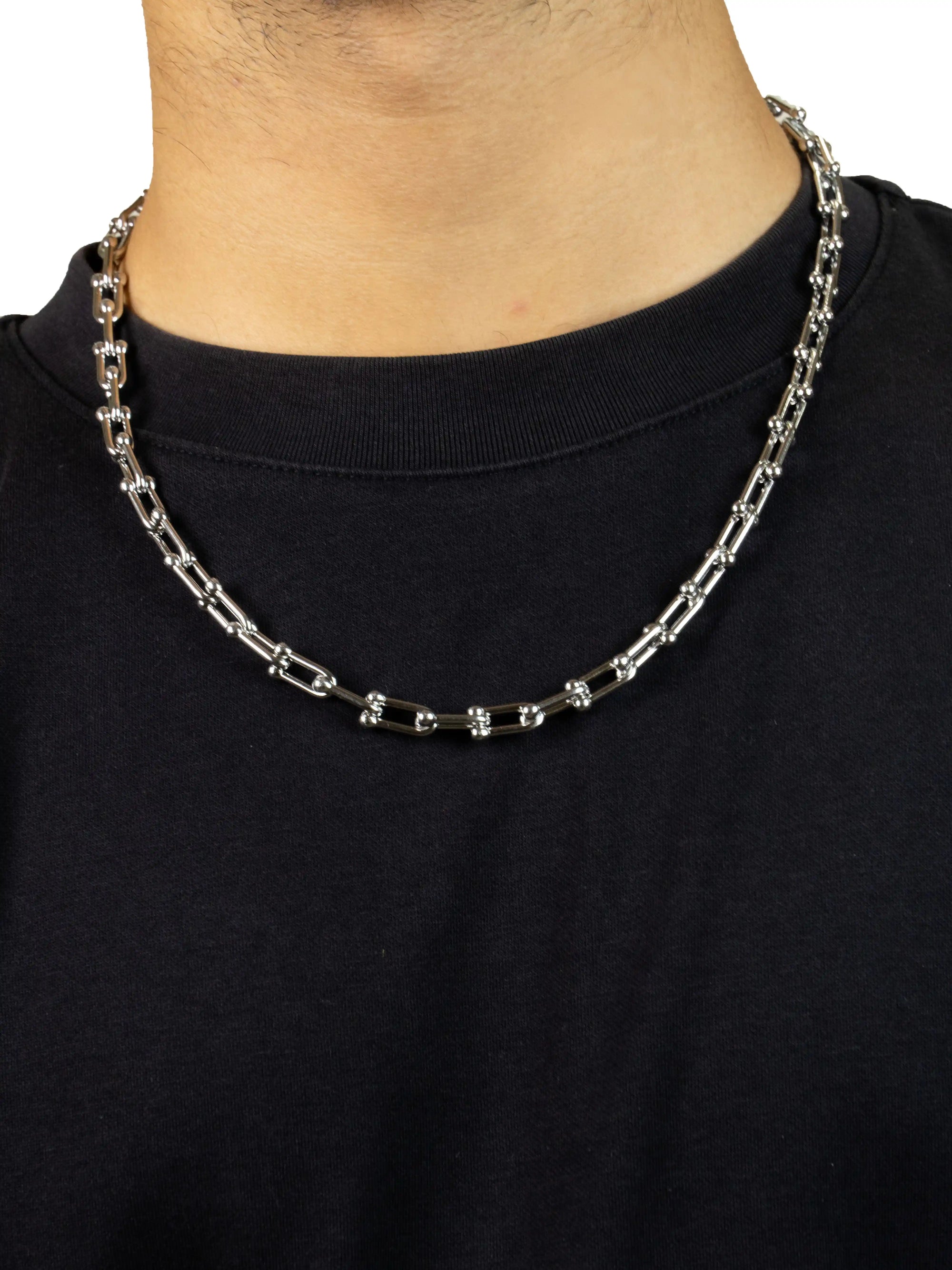 Silver chain necklace worn by a person on a black shirt background