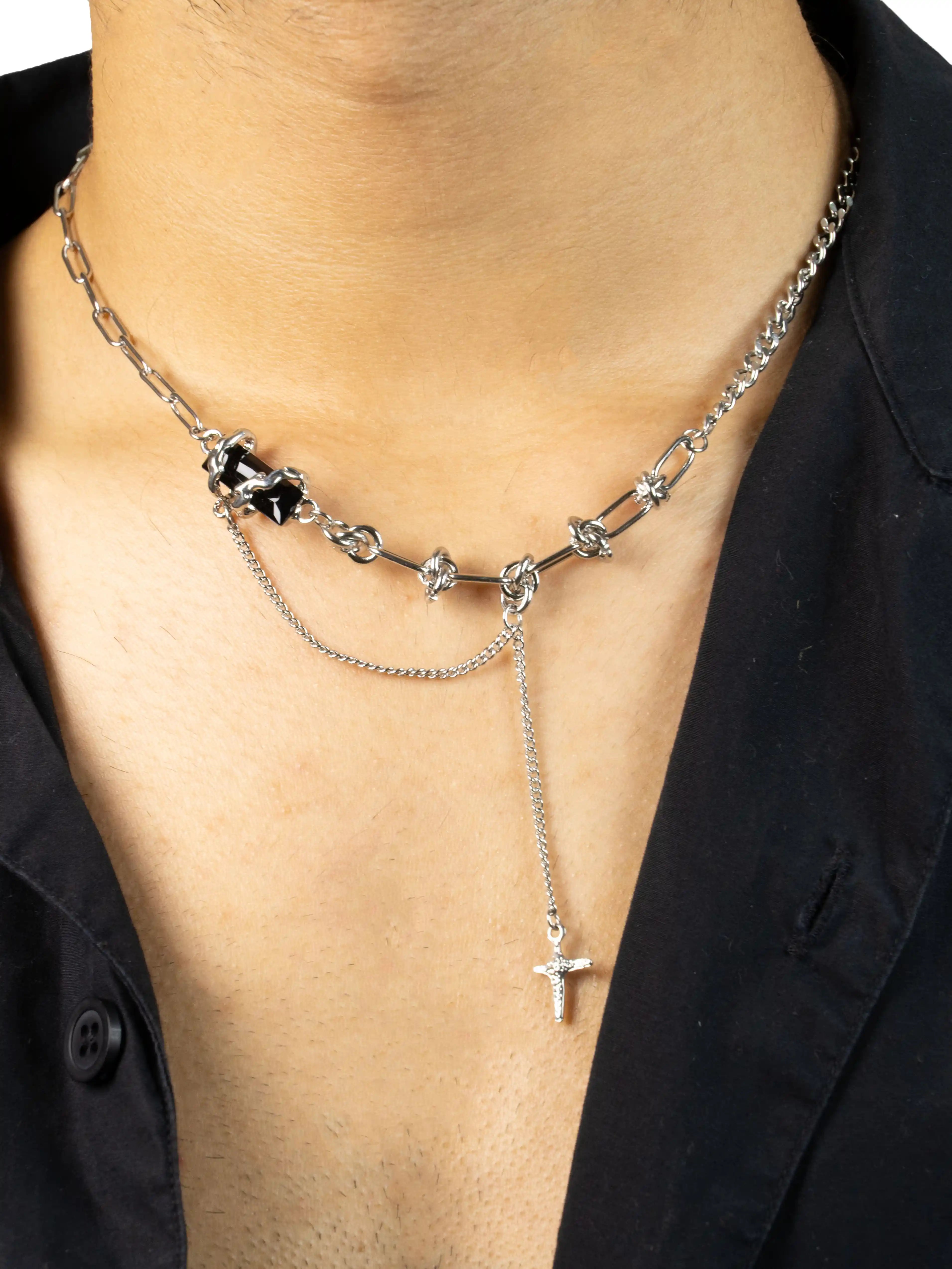 Silver necklace with a cross pendant on a person wearing a black shirt.
stawp