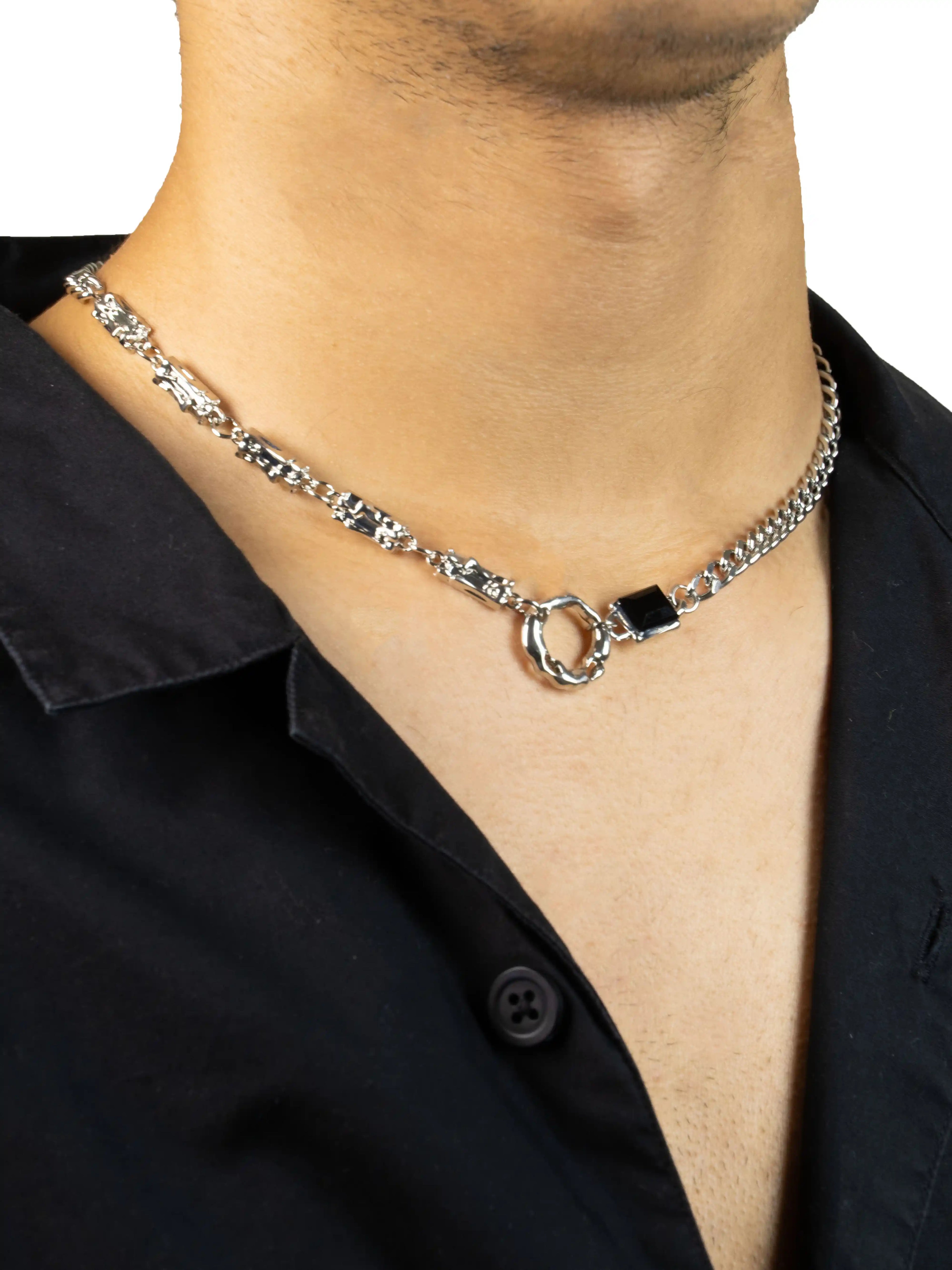 Silver chain necklace with a black accent worn by a person in a black shirt.
stawp