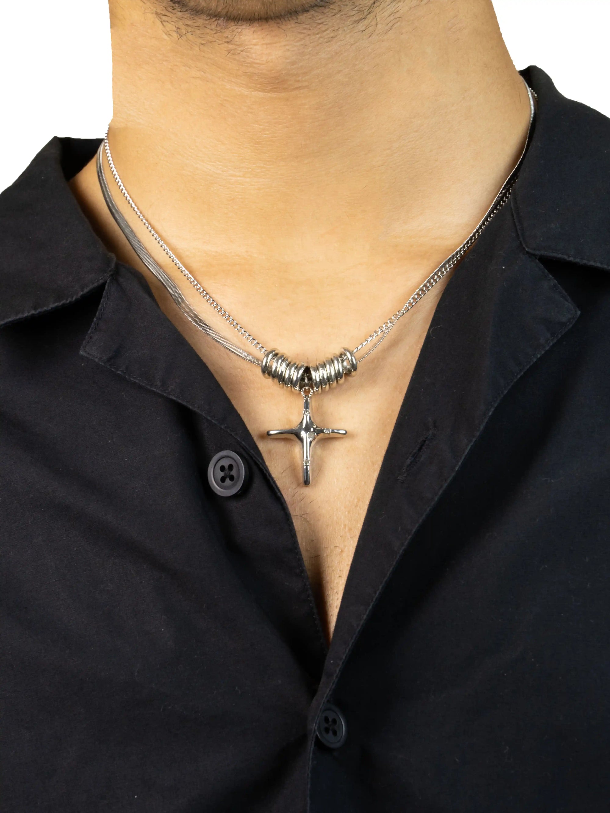 Silver necklace with a cross pendant worn by a person in a black shirt.
stawp