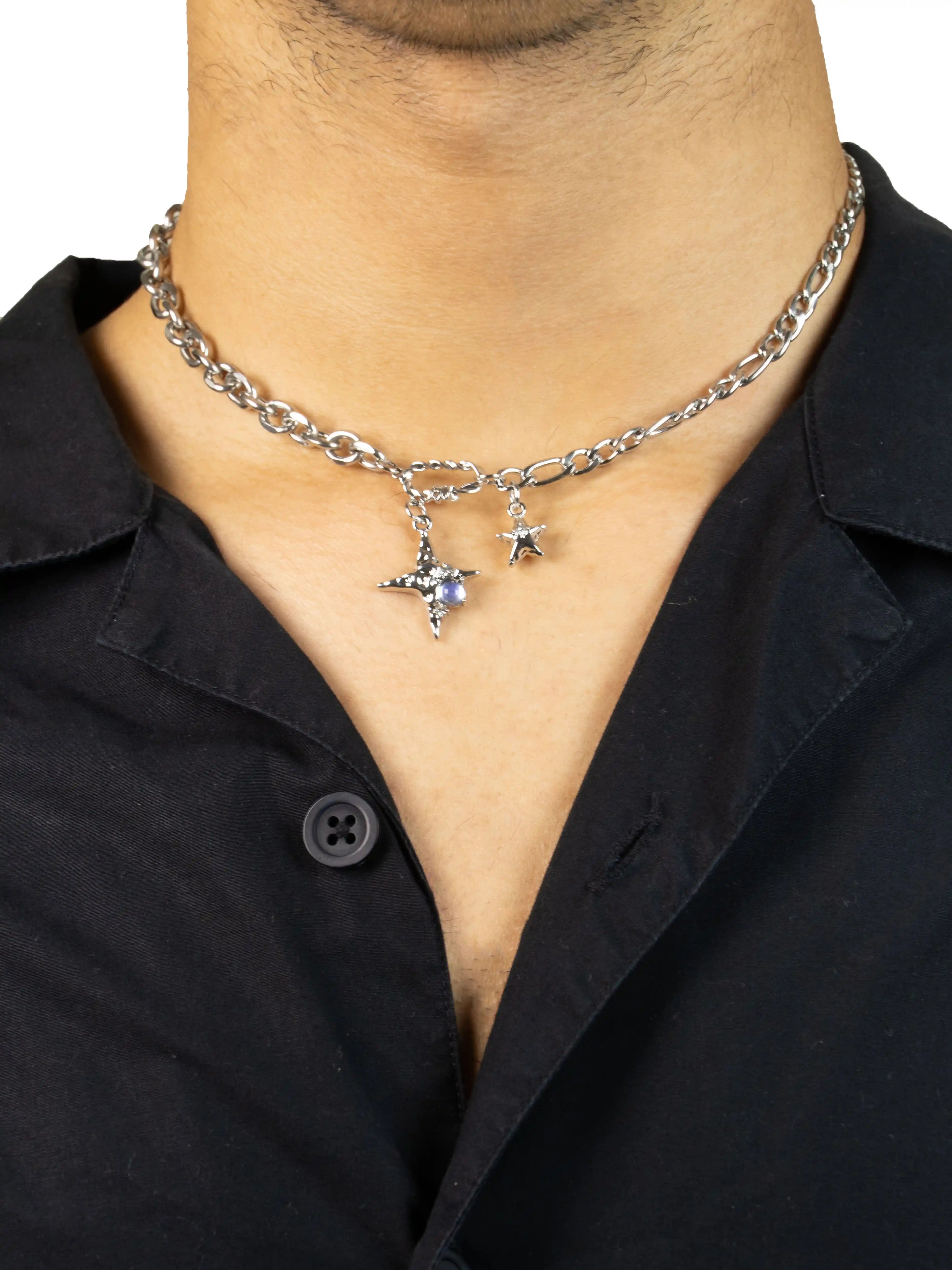 Person wearing a silver chain necklace with star pendants on a black shirt.stawp