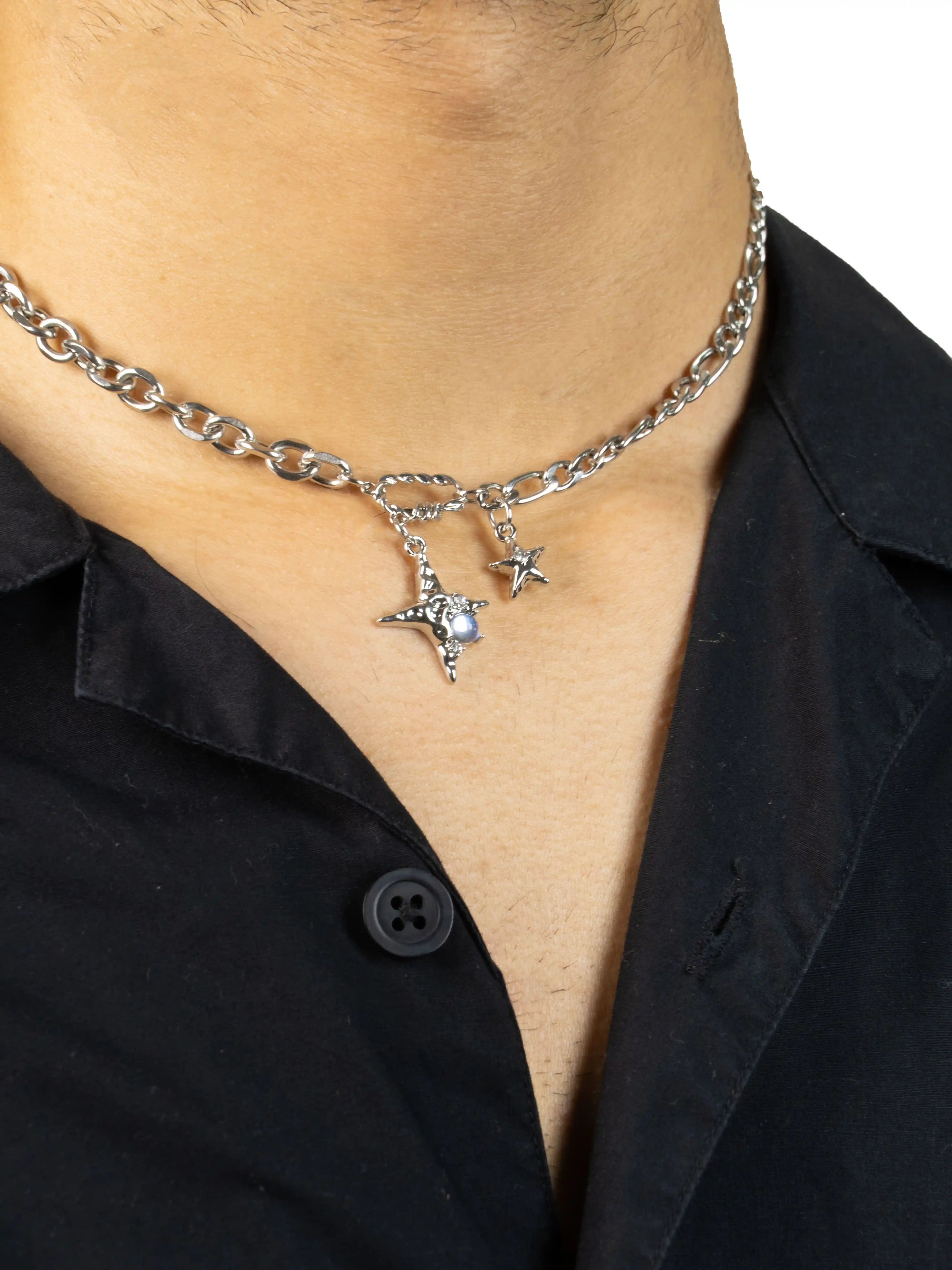 Silver chain necklace with star pendants worn by a person in a black stawp shirt.