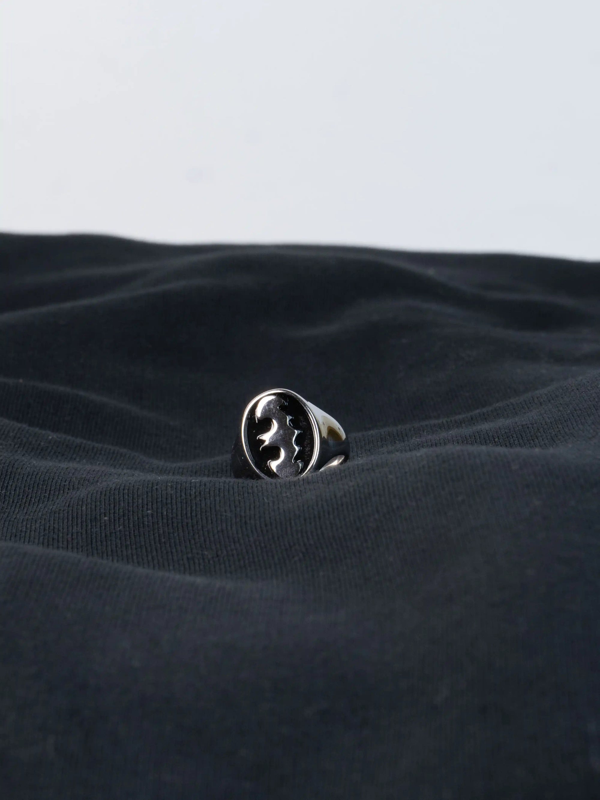 Silver ring with batman logo on a textured black fabric background