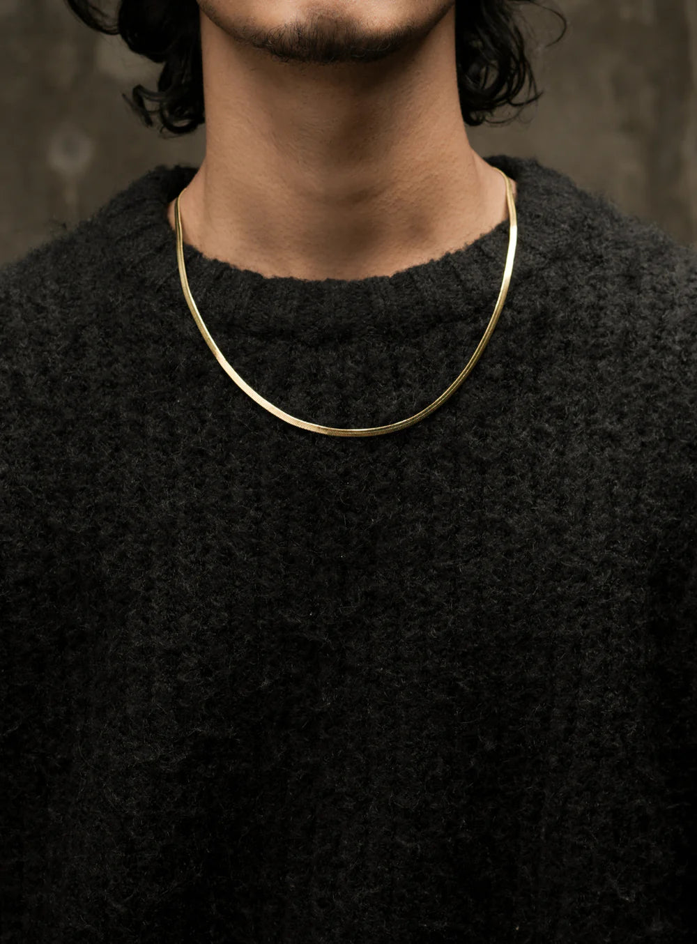 Golden Foxtail chain necklace by Stawp, worn by a model in a black textured sweater. The chain curves naturally around the model’s neck, displaying its sleek, flat design and refined gold color.