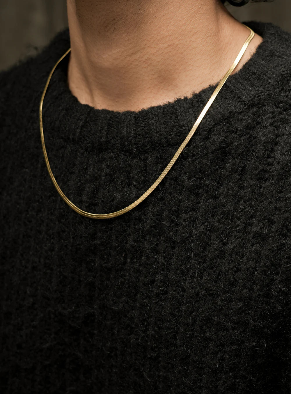 Close-up of the Golden Foxtail chain necklace by Stawp, highlighting its polished finish and subtle shine as it rests on the model’s neck, paired with a black textured sweater
